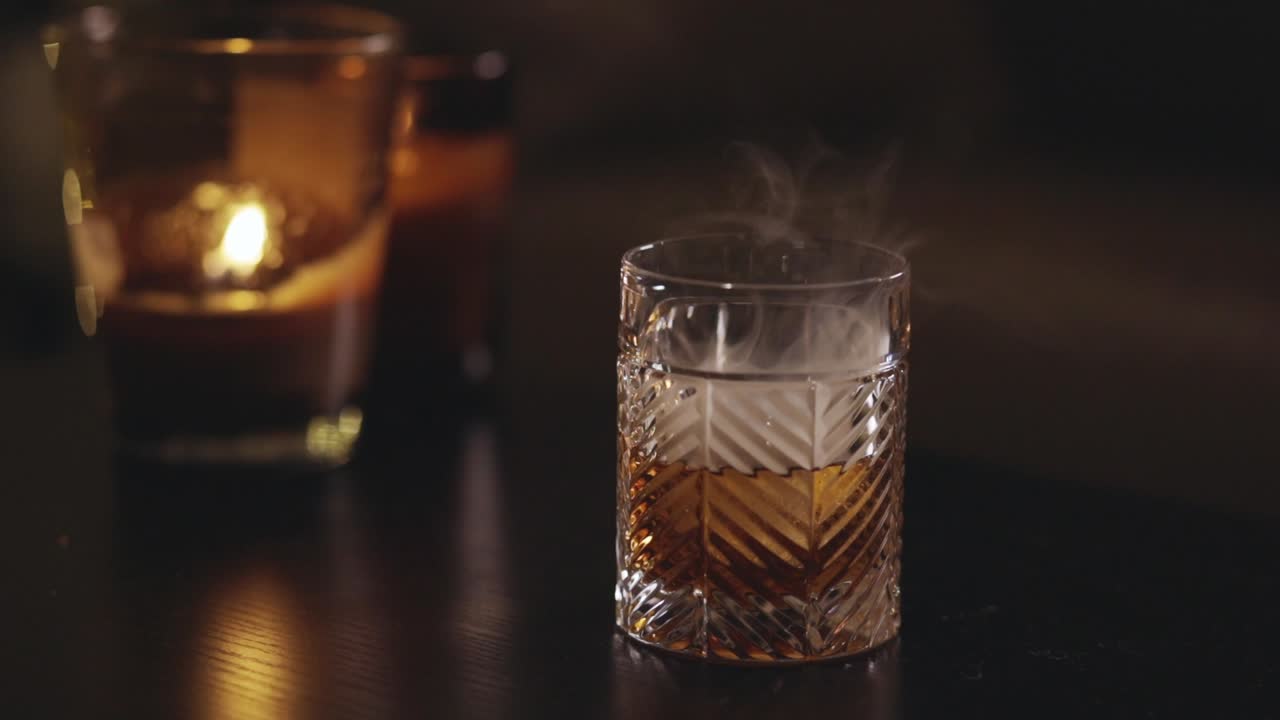 Barman quita la tapa de madera del vaso con whisky y humo. - Primer plano.