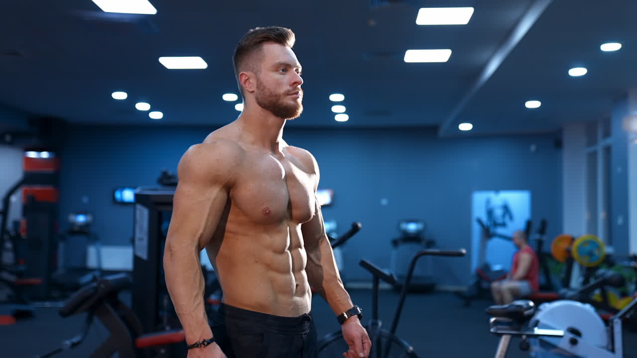Hot handsome strong guy man without a shirt against gym background. Male beauty concept. Slow motion.