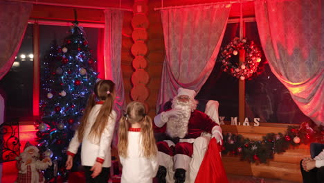 Santa Claus and kids in the house. Happy Santa with white beard sits into armchair and listen to children. Christmas decorated room background.
