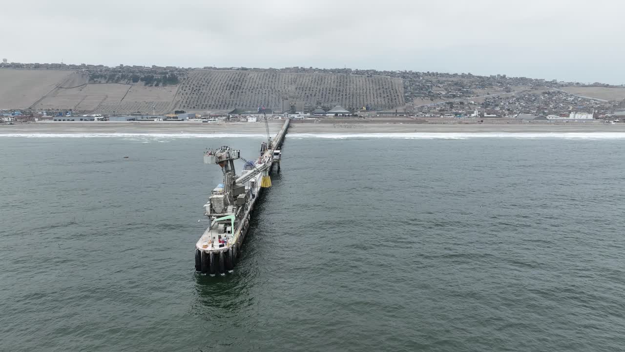 페루 리마의 푸쿠수나 해변에 있는 우남 대학 부두에서 부서지는 파도와 건물이 있는 풍경을 바라보며 해변으로 날아가는 공중 돌리