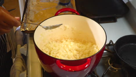 mujer agrega ingredientes a las cebollas en una olla para base de chile, cierre lento