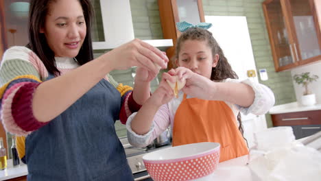 madre y hija bi-raciales felices preparando masa y sonriendo en la cocina soleada