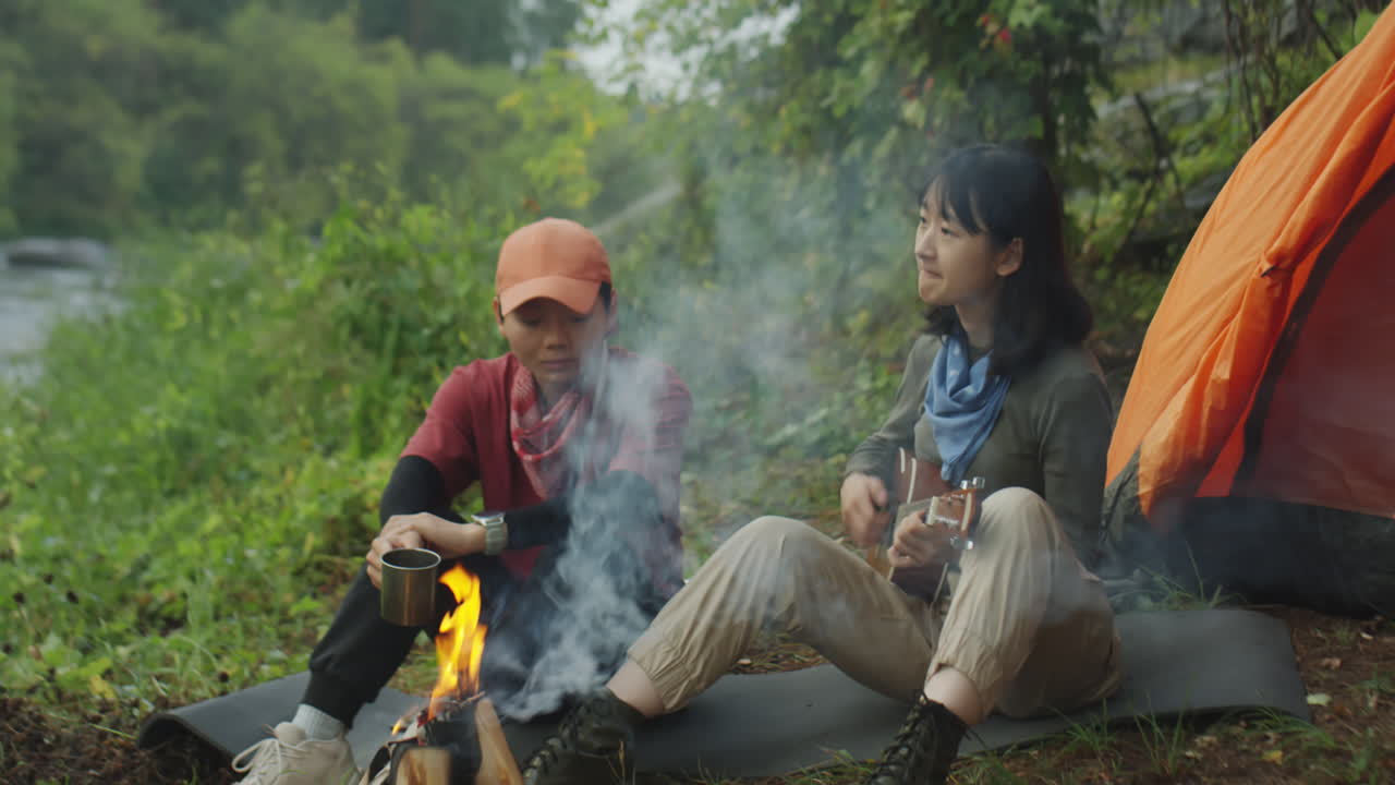 Girls Having Tea and Playing Guitar by Campfire