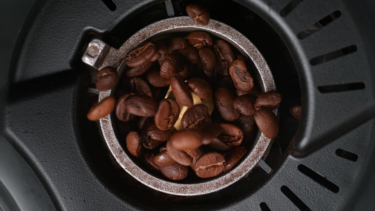 los granos de café tostados caen en el molinillo de burr lentamente siendo molidos, vista de arriba