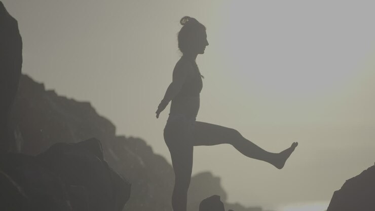 Woman practicing yoga on a rocky beach at sunrise