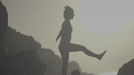 woman practicing yoga on a rocky beach at sunrise