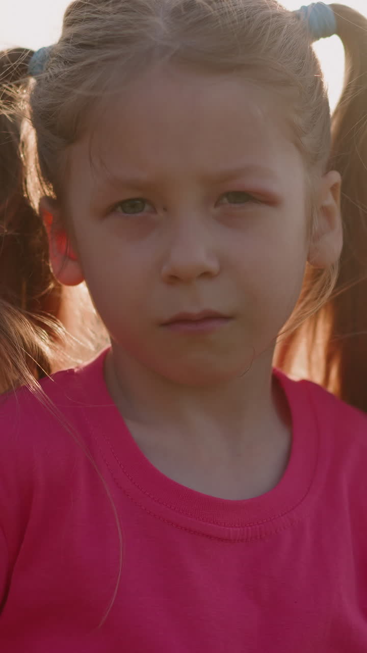 Sad junior schoolgirl with injured eye looks in camera on lawn slow motion. Victim of school bulling. Destructive relationship with classmates