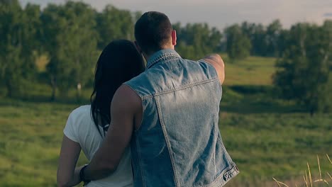 close backside view young couple stands against green trees