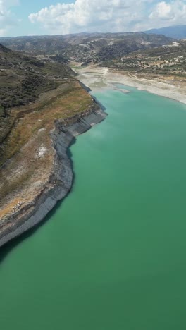 a vertical drone capture reveals the grandeur of kouris dam, emphasizing its vast reservoir, winding edges, and the surrounding rugged terrain in stunning detail.