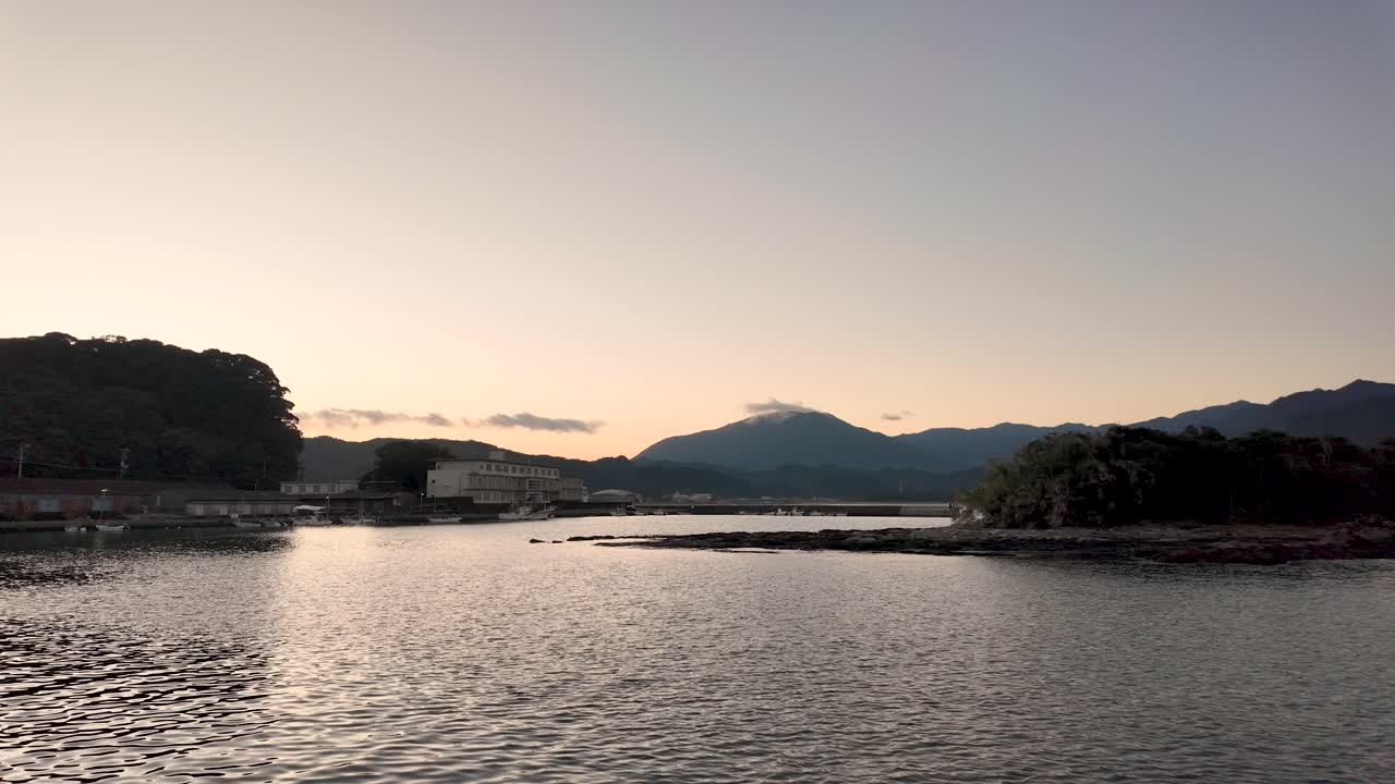 Evening light casts a serene glow over Nachi Bay, with calm waters reflecting the distant mountains under a peaceful sky