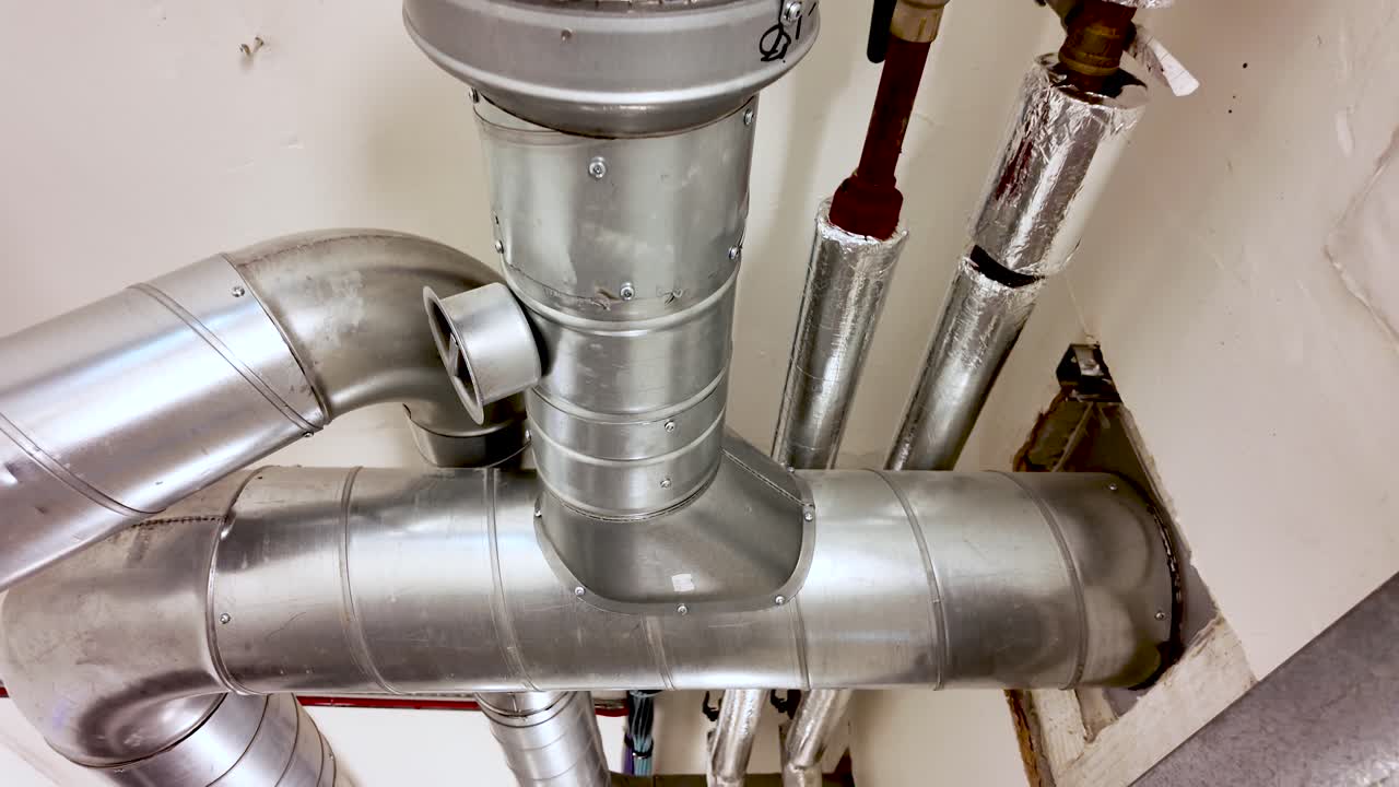 Sistema di ventilazione industriale con tubi e condotti metallici visibili su un soffitto bianco.
