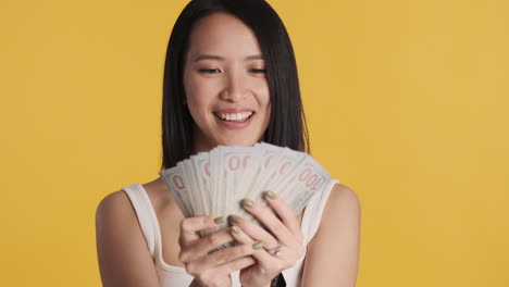 asian woman looking happy while holding money on camera.