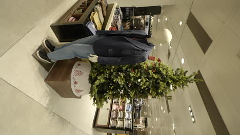 Vertical-interior-shot-of-shopping-mall-with-Christmas-decorations-tree,-clothes