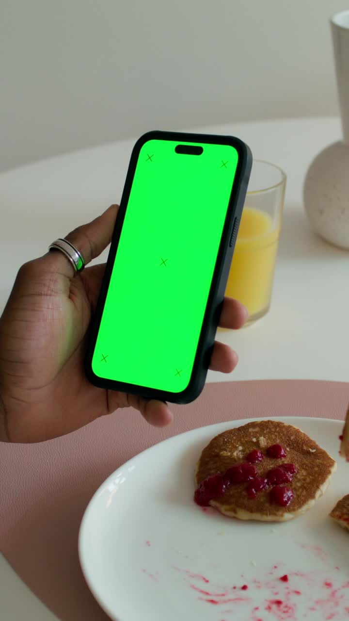 persona sosteniendo un teléfono con pantalla verde en la mesa del desayuno con panqueques