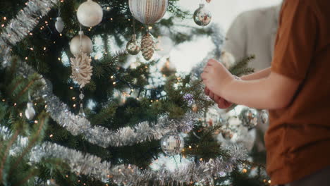 young boy puts baubles on the christmas tree