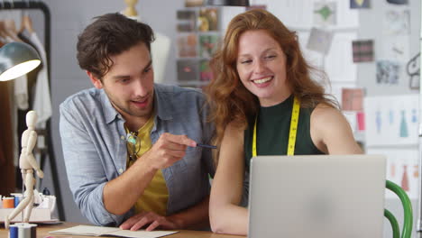 male and female clothes designers working on designs using laptop in fashion studio