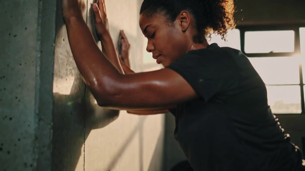 Starting lunge athlete leaning into wall on gym mat in sportswear barefoot with dumbbell for warmup