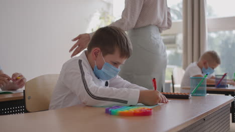 grupo multirracial de niños con máscaras faciales trabajando en clase escribiendo y escuchando las explicaciones del maestro en el aula