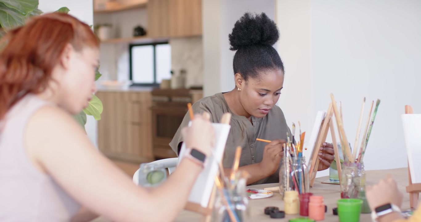 African American women painting at kitchen table dipping brushes mixing palette colors creating art