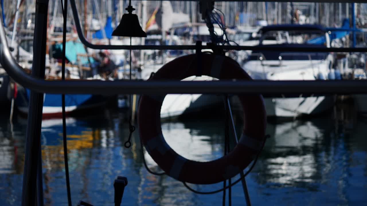 Campana y salvavidas de un barco con yates borrosos amarrados al fondo, Alicante, España.