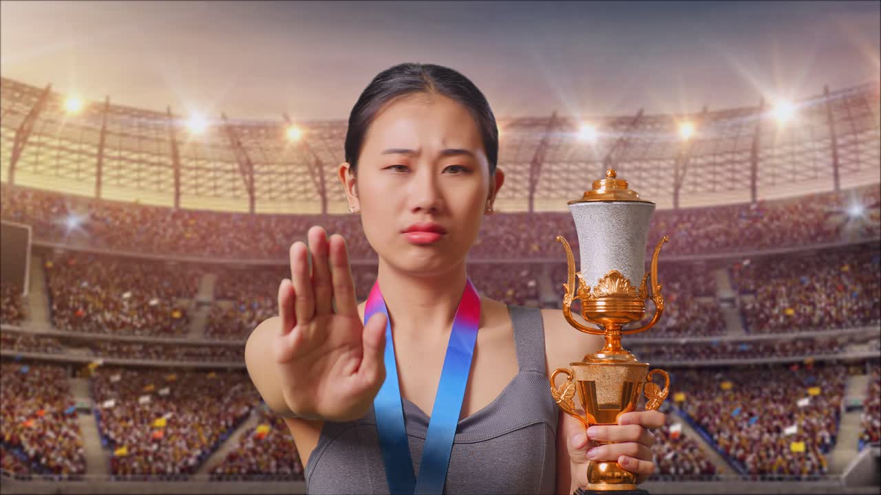 Close Up Of Asian Woman With A Gold Medal And Trophy Disapproving With No Hand Sign And Smiling To Camera At The Stadium