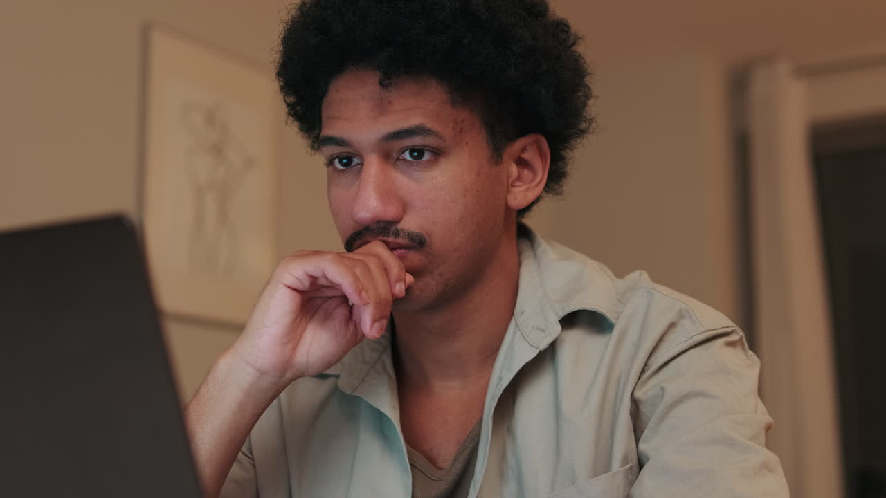Young Man with Afro and Mustache Working Thoughtfully on Laptop