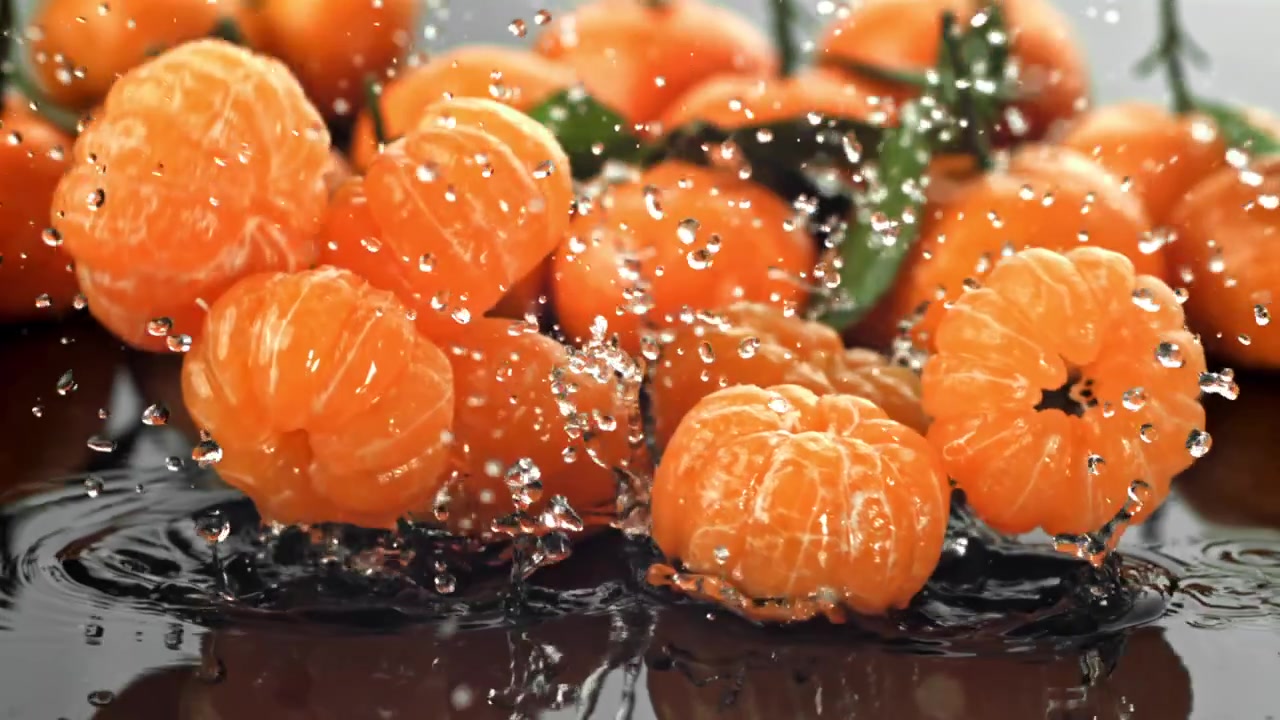 Skrelte mandarinskiver plasker ned i vann i sakte film