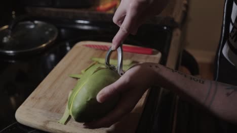 a woman at the kitchen carefully peeling an unripe mango using a metal peeler - close up shot