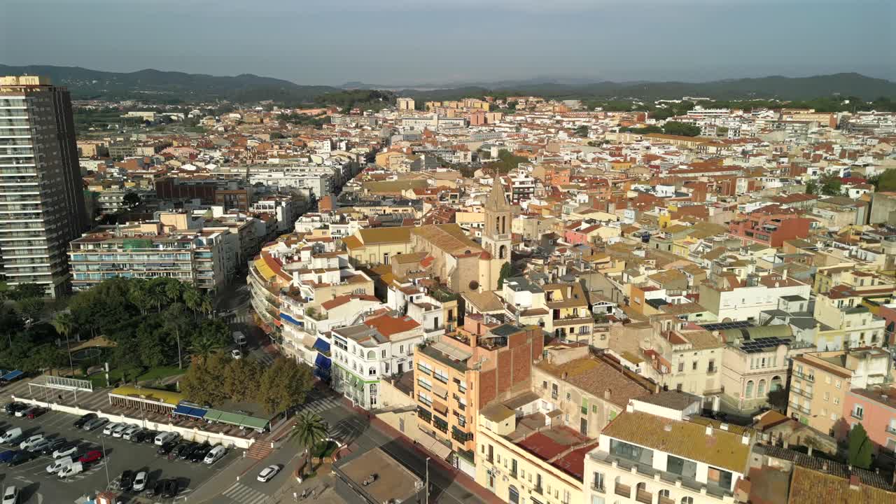 Ripresa aerea 4K con drone a Palamos, Spagna, che vola all'indietro dalla chiesa cittadina verso il porto e la spiaggia. Movimento inverso fluido con un'ampia vista del villaggio costiero, paesaggio mediterraneo e tetti.