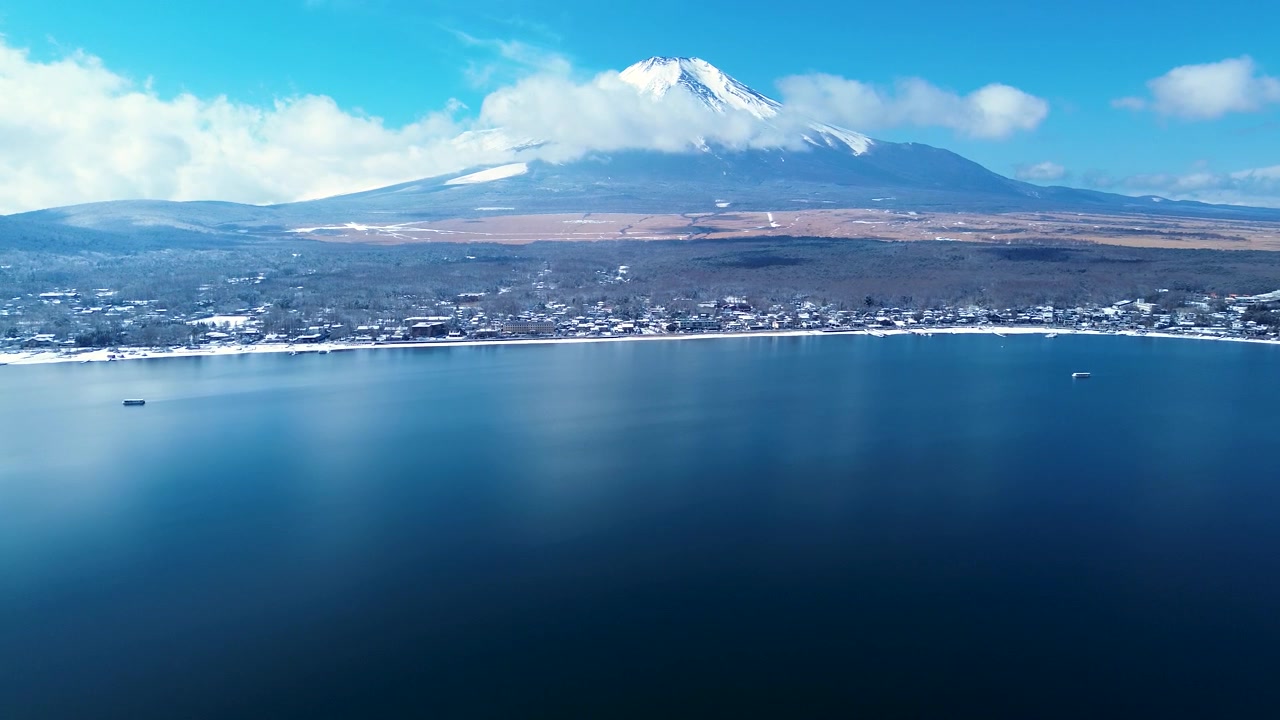Paisaje aéreo con dron de la cima nevada del Monte Fuji, cubierta de nubes brumosas, con vistas al sistema de vías fluviales del lago Yamanaka y los suburbios de pueblos rurales en el distrito de Minamitsuru, Yamanashi, Japón. Turismo en Asia.