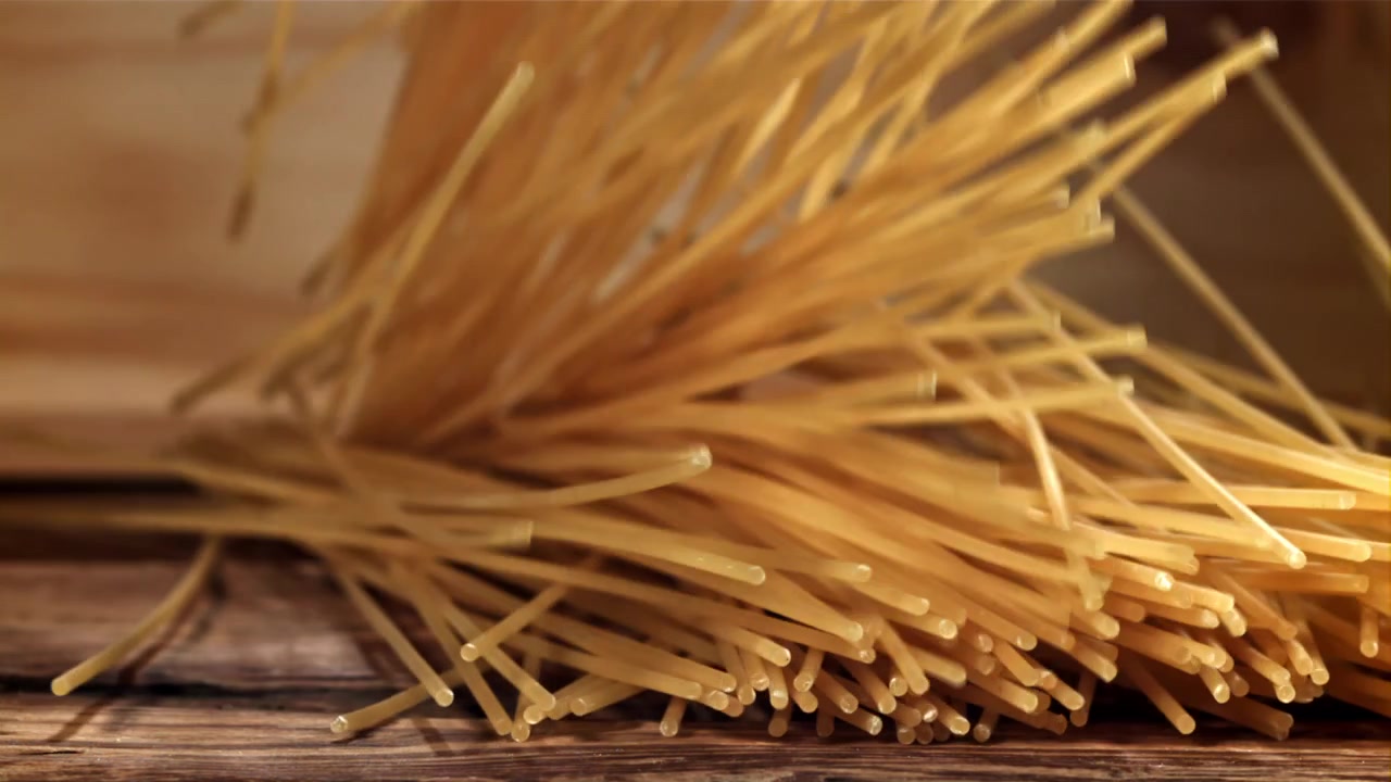 Espagueti crudo cayendo a cámara lenta sobre una mesa de madera