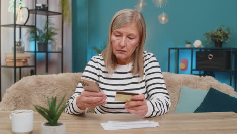 mature woman using credit card and smartphone to transfer money pay bills sitting on table at home