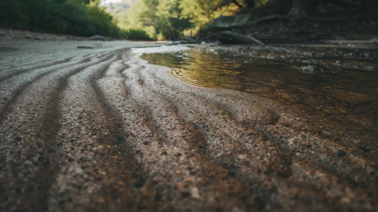 Ripresa dal basso con camera bagnata su sabbia increspata e torrente poco profondo che traccia l'increspatura, mostrando la texture al torrente