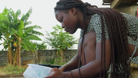 Cleaning-plastic-wares-with-dishwashing-soap-and-a-scouring-pad,-a-local-woman-is-doing-her-chores-outside-of-her-house-in-a-village-in-Kumasi,-Ghana,-Africa