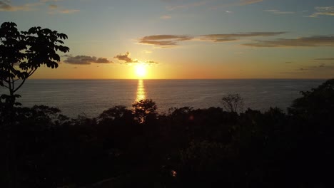 Un-Dron-Aéreo-Captura-El-Esplendor-Del-Atardecer-En-La-Playa-De-Uvita-En-Costa-Rica-Mientras-Se-Desplaza-Lentamente-Hacia-La-Izquierda:-Un-Encantador-Sol-Anaranjado-Proyecta-Su-Brillo-Sobre-El-Mar,-Revelando-Una-Vibrante-Belleza-Natural