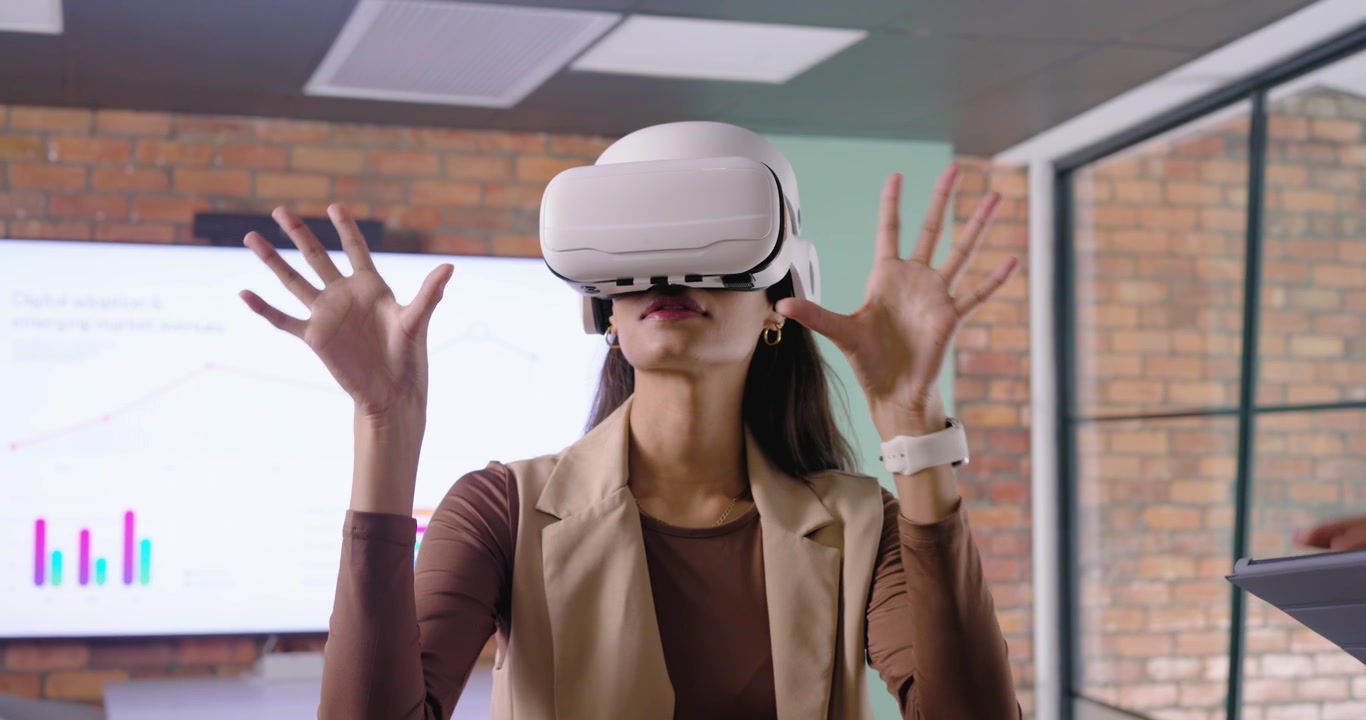 Donna di un team eterogeneo con gilet beige che testa un visore VR, guidata da un uomo che usa un tablet in ufficio
