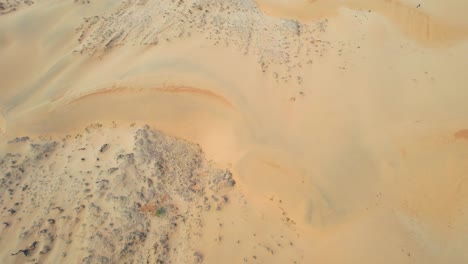 panorámica aérea hacia abajo del paisaje de dunas de arena secas y rocosas en el desierto