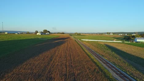 a drone view of crops waiting to be harvested as a stream passenger train approaches during the golden hour on a fall day