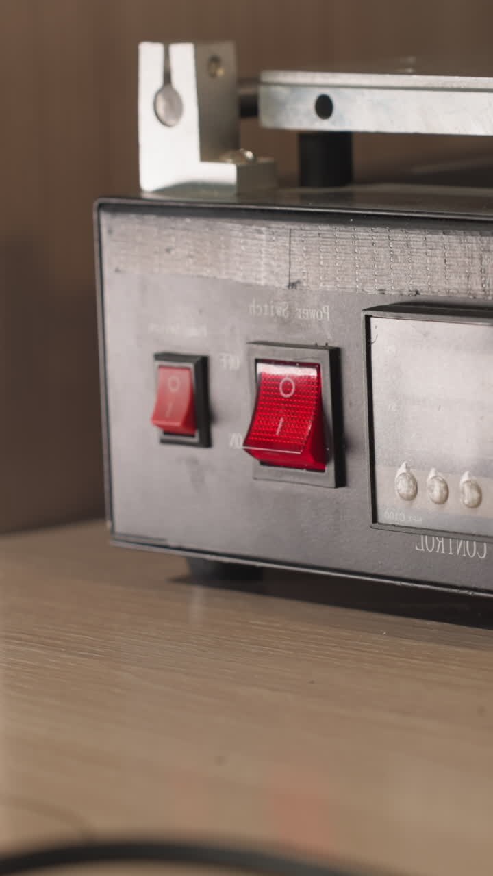 A close-up view of a technician in black gloves pressing a red power switch on a temperature control device