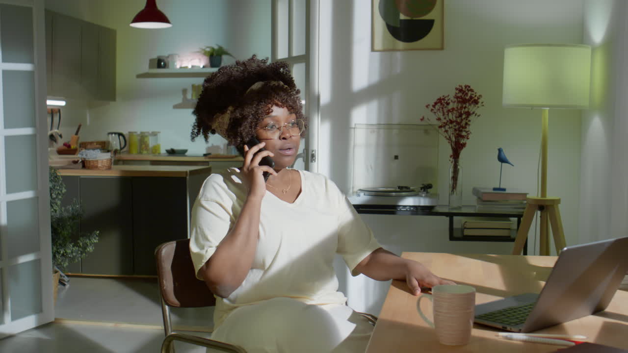 Sort kvinde taler i telefon, mens hun arbejder derhjemme