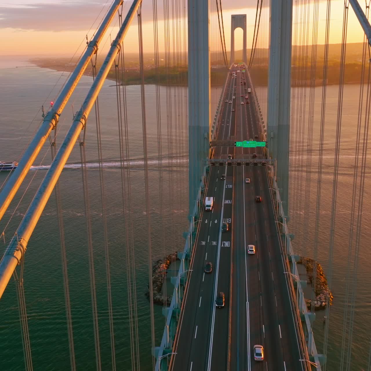 New York Whitestone bridge with cars moving along. Sunset over the river and boat sailing under the bridge