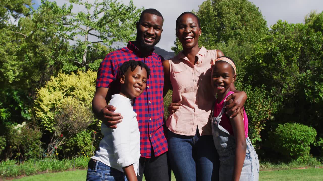 портрет улыбающихся афроамериканских родителей, обнимающихся с сыном и дочерью в саду