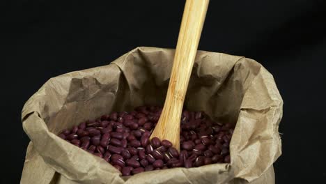 los nutritivos frijoles rojos secos de adzuki giran en una bolsa de papel con una cuchara de madera