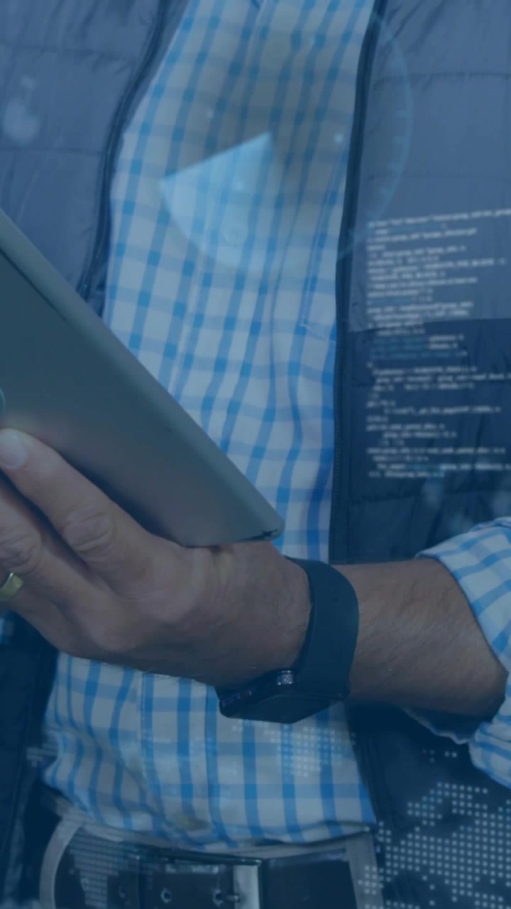 Vertical video: Man tapping tablet, making tech code overlay while camera rising, reviewing data