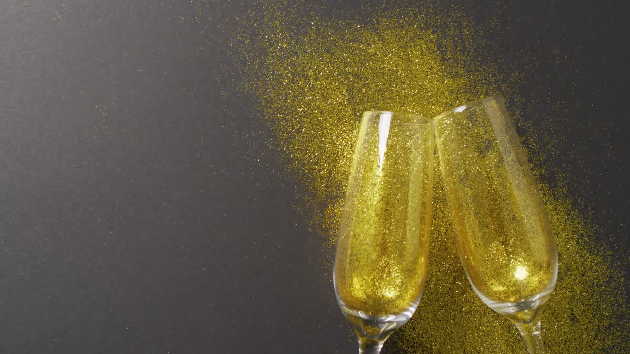 Video di due flûte di champagne con brillantini dorati su sfondo nero, con spazio per il testo.