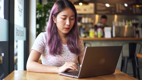 young woman with purple hair working on laptop at cafe