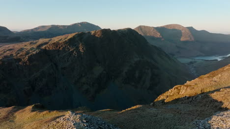 montañas al amanecer con vuelo sobre el borde del acantilado revelando valle oscuro y lago lejano