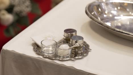 set of holy oils, water, and towel prepared for a baptism or sacramental ceremony on a silver tray