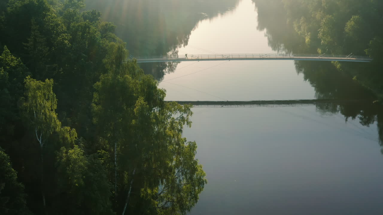 백패커는 화창한 날 강 위의 다리를 건너고 드론을 쏘았습니다.