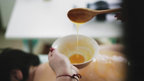 therapist with liquid honey near patient on couch at massage